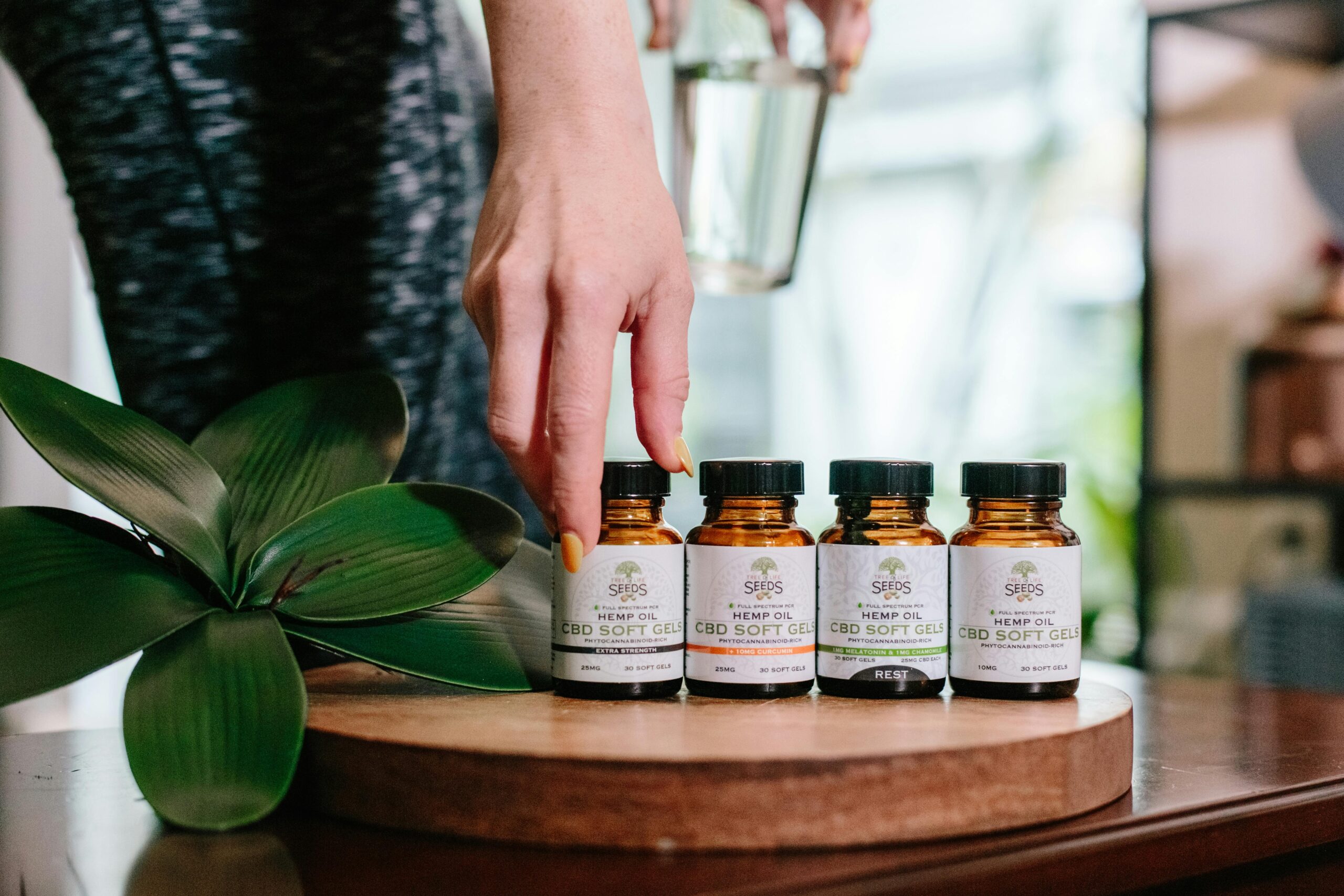Close-up of CBD soft gel bottles with a hand picking one up. Indoor setting.